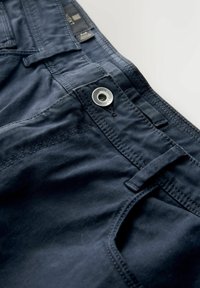 Dunkelblaue Jeansnahaufnahme, die den Knopf, die Gürtelschlaufen, die Nähte und die Textur des Stoffes auf einem hellen Hintergrund zeigt.