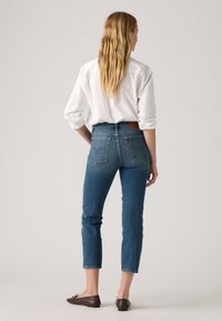 Aukštai iškilę mėlyni džinsai su išblukusiu plovimu, prigludusi forma ir trumpa kulkšnies ilgio dalimi. Rudas odinis užrašas gale, ant juosmens.