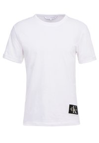 Biała bawełniana koszulka z krótkim rękawem, okrągłym dekoltem oraz czarną prostokątną łatą z logo w lewym dolnym rogu.