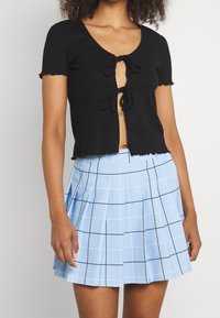 Top corto negro de canalé con mangas cortas y cierre delantero de lazo, combinado con una falda plisada de cuadros azul claro que presenta líneas en cuadrícula negras.