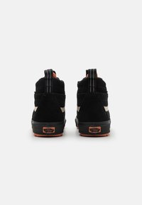 Sorte semskede høyhælte sneakers med oransje detaljer, teksturert såle, stripede hæltrekk og distinkt merkepute på hælen.