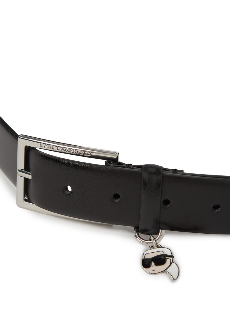 Schwarzer Leder-Gürtel mit einer metallischen eckigen Schnalle und Etikett. Verfügt über einen dekorativen Charm in Form eines Kopfes mit Sonnenbrille, der am Riemen befestigt ist.