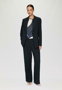 Black tailored suit jacket and wide-leg trousers paired with a geometric printed blouse in navy, cream, and light blue. Square sandals.