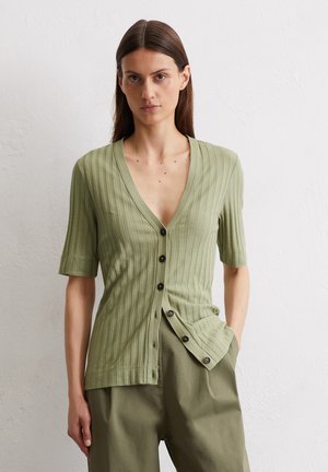 Gilet côtelé vert clair à manches courtes, décolleté en V profond, boutons sur le devant et texture subtile, associé à un pantalon ample assorti.