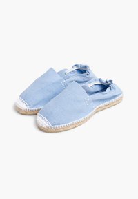 Espadrilles en tissu bleu clair avec une semelle en jute tissée plate, un bout rond et un dos élastiqué. Présente des coutures blanches sur les bords.