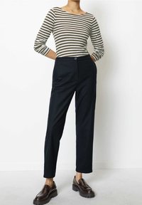 Randig långärmad topp i olivgrön och krämfärgad, parat med högmidjade, slim-fit svarta byxor med knappstängning och sidofickor.