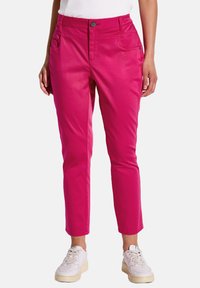 Pantalons en coton mélangé rose avec une coupe slim, dotés d'une fermeture à bouton, d passants de ceinture et de poches avant. Portés avec des baskets blanches.