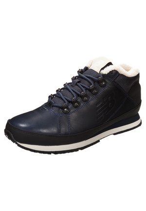 Botte d'hiver en cuir et tissu bleu foncé avec semelle noire, bande blanche sur la semelle intermédiaire, œillets métalliques noirs, lacets bleu marine et doublure en polaire blanche.