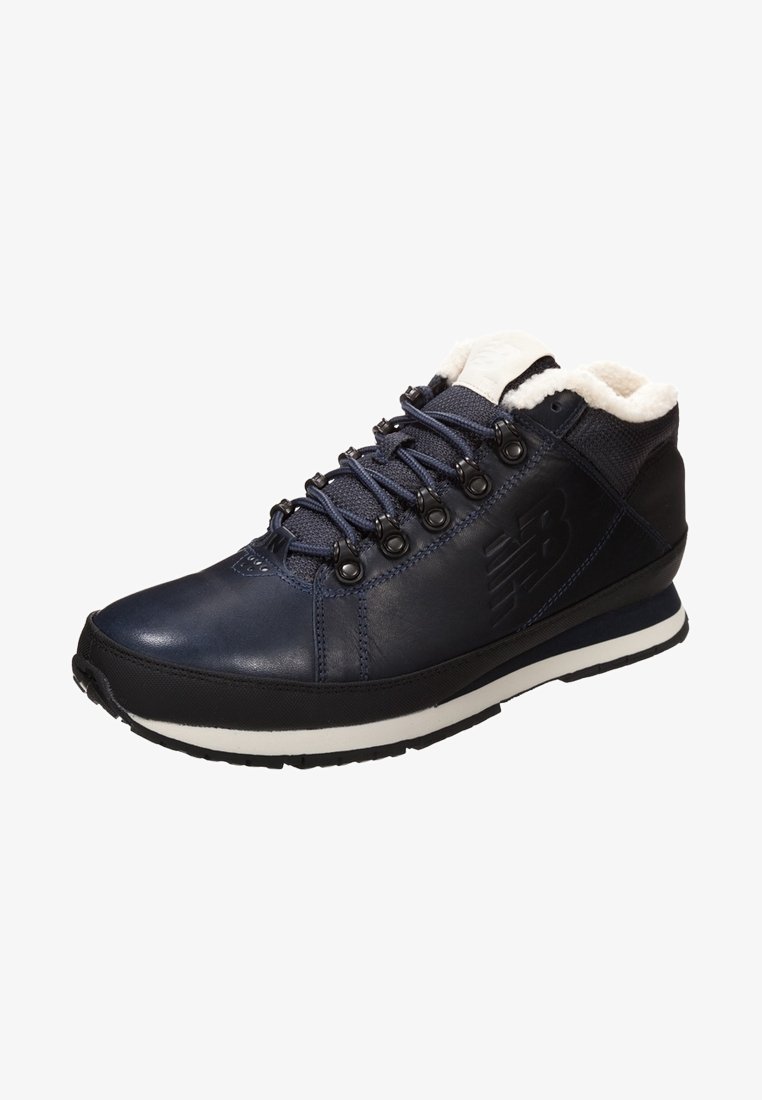Botte d'hiver en cuir et tissu bleu foncé avec semelle noire, bande blanche sur la semelle intermédiaire, œillets métalliques noirs, lacets bleu marine et doublure en polaire blanche.