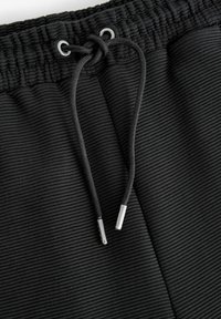 Sort shorts lavet af tekstureret stof, der har en bred elastisk talje, snor med metalspidser og vertikal ribbenmønster.