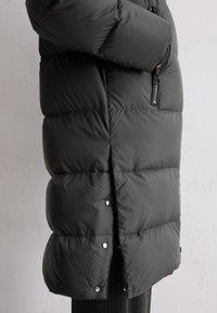 Schwarze Steppjacke mit einem gesteppten Design, Reißverschluss-Seitentasche und Druckknöpfen am Saum. Glatte Nylon-Oberfläche, mittellang.