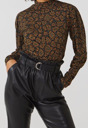 Donna che indossa una maglia a maniche lunghe con stampa leopardata infilata in pantaloni neri in pelle a vita alta con una cintura larga e le mani nelle tasche.