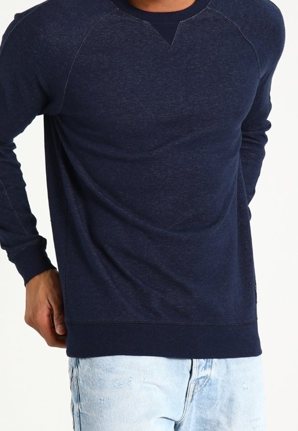 Sudadera de cuello redondo en azul marino con mangas raglán, hecha de una tela suave. Presenta un cuello y puños acanalados, combinada con unos jeans de mezclilla azul claro.