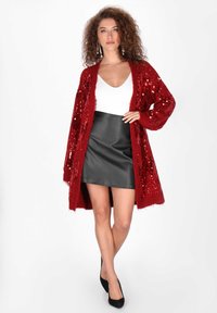 Czerwony kardigan z cekinami, z długimi rękawami, otwarty z przodu i o puszystej fakturze, w połączeniu z czarną skórzaną mini spódnicą i czarnymi szpilkami.