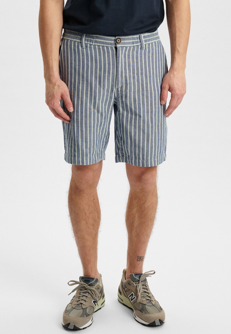 Blauw-witte gestreepte shorts van katoen, met een knoopsluiting en een rechte snit, gecombineerd met grijze sneakers.