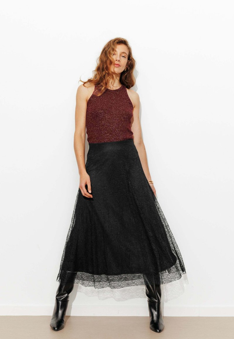 Haut dos nu bordeaux en tissu texturé associé à une longue jupe en dentelle noire. La tenue est mise en valeur par des bottes noires ajustées.
