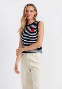 Top senza maniche a righe navy e bianche con ricamo di un cuore rosso, abbinato a pantaloni a gamba larga color crema chiara. Materiale in maglia morbida.
