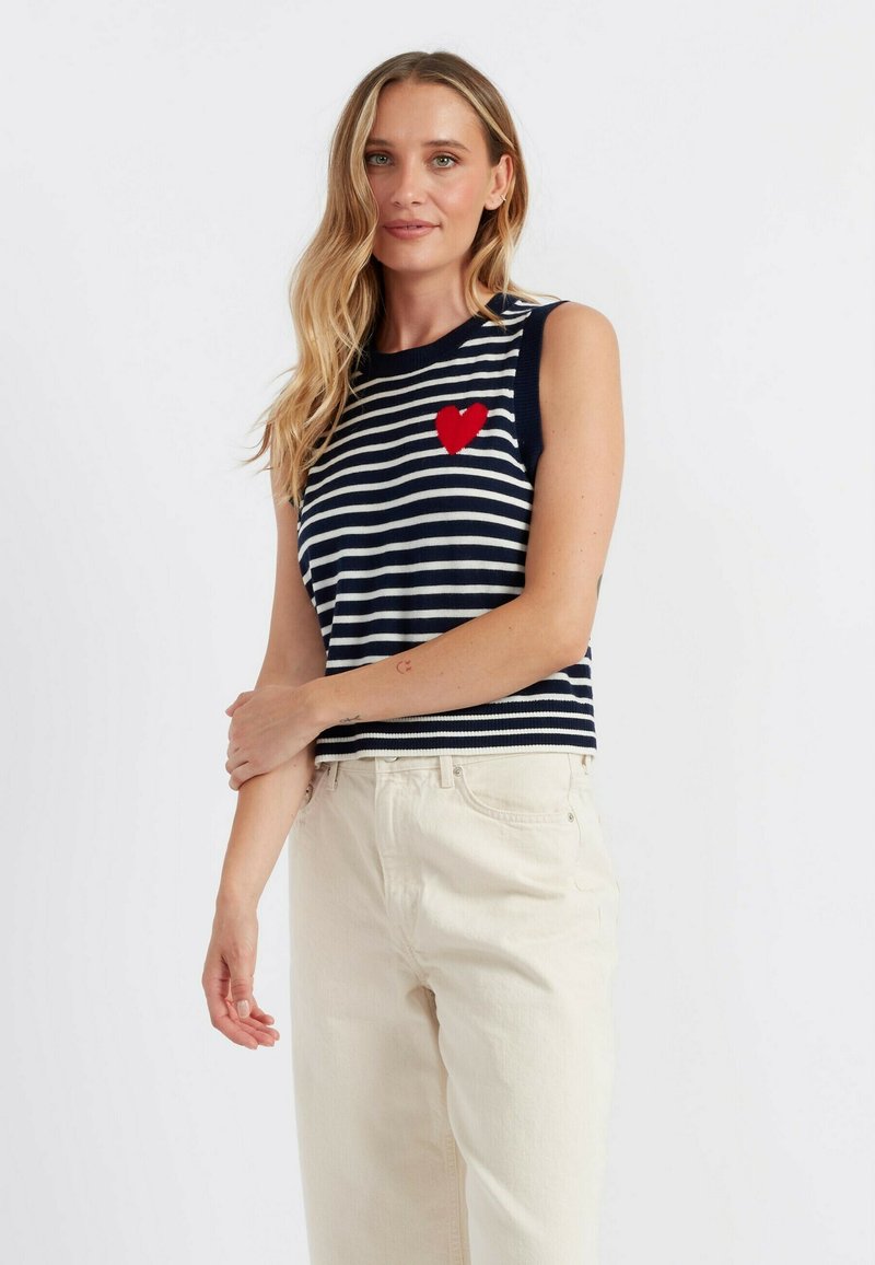 Top senza maniche a righe navy e bianche con ricamo di un cuore rosso, abbinato a pantaloni a gamba larga color crema chiara. Materiale in maglia morbida.