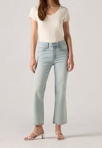 Jeans de mezclilla azul claro con corte recto, talle alto y lavado desgastado. Combinados con una camiseta blanca ajustada y acanalada, y sandalias minimalistas.