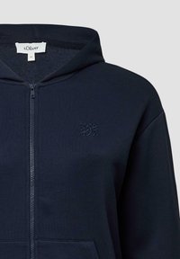 Marineblauwe zip-up hoodie van zachte stof, voorzien van een kangoeroezak en een geborduurd logo op de borst. Gladde textuur en een relaxte pasvorm.