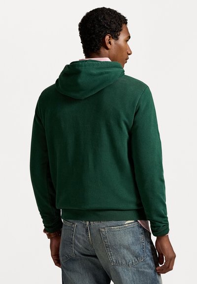 Groene hoodie met een zachte textuur, geribde manchetten en een kangoeroezak, gecombineerd met versleten blauwe spijkerbroeken.