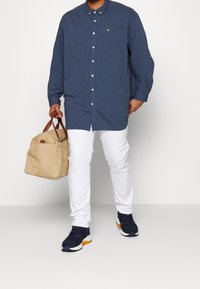 Niebieska koszula na guziki z kieszenią na piersi, białe spodnie, ciemne trampki z pomarańczowymi akcentami oraz beżowa torba z brązowymi uchwytami.