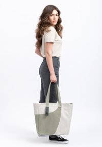 Borsa tote in canvas con un design bicolore in grigio chiaro e verde oliva, dotata di manici robusti e di un'etichetta cucita distintiva.
