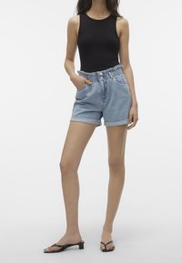 Jeansshorts med en ljusblå tvätt, elastisk midja, knappstängning fram och upplottad fåll. Bärs med en svart ärmlös bodysuit och svarta sandaler.