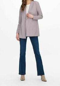 Blazer lungo viola chiaro con revers, indossato sopra una maglietta bianca. Abbinato a jeans a zampa d'elefante blu e stivali alto beige.