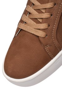 Hnědá kožená teniska s béžovými tkaničkami, bílou gumovou podrážkou, viditelným prošíváním a texturovaným povrchem kůže.