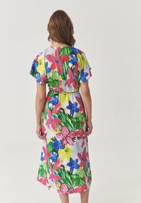 Bloemige jurk met een levendig patroon van roze, blauwe en groene bloemen, korte mouwen en een knoop tailleontwerp. Zachte, lichte stof.