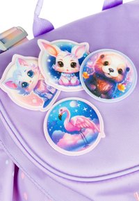 Quattro adesivi circolari colorati con animali dei cartoni animati e un fenicottero su uno zaino a trama lilla.