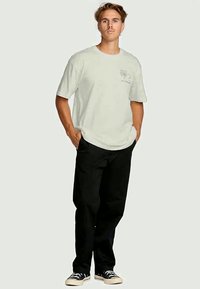 Lichtgroene t-shirt met korte mouwen en een palmbomenafbeelding, gecombineerd met zwarte broek en zwart-witte sneakers. Eenvoudig ontwerp, relaxte pasvorm.
