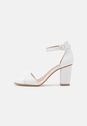 Hvid åben tå-højhælet sandal med ankelrem og spænde, chunky hæl og glat læderfinish.