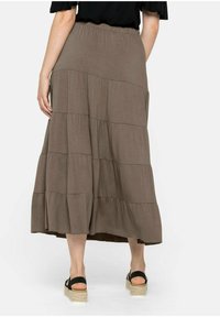Falda maxi marrón de capas, hecha de una tela suave; presenta una cinturilla elástica y un diseño fluido, combinada con sandalias de plataforma negras.