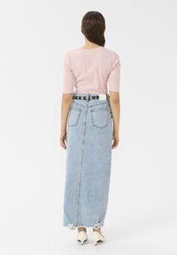 Light pink fitted top with three-quarter sleeves paired with a light blue, distressed denim maxi skirt and a black belt with silver accents.