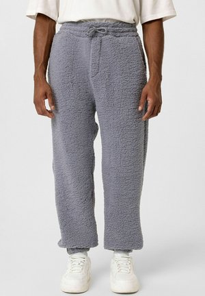 Grijze fleece broek met een gestructureerde oppervlakte, elastische tailleband, verstelbaar trekkoord en recht design, gecombineerd met witte sneakers.