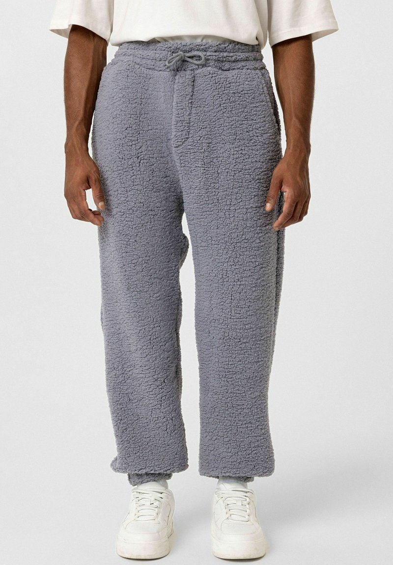 Grijze fleece broek met een gestructureerde oppervlakte, elastische tailleband, verstelbaar trekkoord en recht design, gecombineerd met witte sneakers.