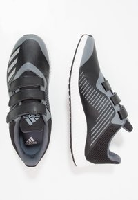 Baskets de sport noires et grises avec trois sangles, tige texturée, panneaux en maille et semelle blanche. Présente des bandes emblématiques sur les côtés.