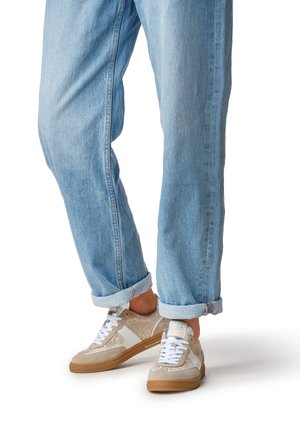 Zapatillas beige y blancas con material texturizado, detalles suaves de ante y suela de goma color topo, combinadas con jeans de mezclilla azul claro remangados.