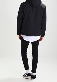 Giacca nera con cappuccio, camicia bianca sotto, pantaloni neri slim-fit, calze bianche, sneakers nere con dettagli rossi. Tessuto morbido, vestibilità casual.