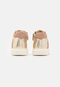 Sneakers z metalicznym złotym wykończeniem, miękkimi różowymi akcentami, z tylnym zapięciem na suwak i białą teksturowaną podeszwą. Zaprojektowane dla dzieci.