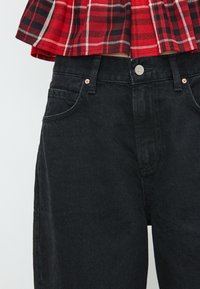 Jeans in denim nero con chiusura a bottone, design a cinque tasche e dettagli in rame. Il tessuto ha una finitura strutturata con una leggera elasticità.