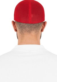 Căciulă roșie din plasă cu un vârf rotund, prezentând un model texturat. Subiectul poartă un tricou polo alb, cu partea din spate a gâtului vizibilă.