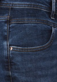 Jeans de denim azul oscuro con costuras visibles, un pequeño bolsillo trasero y un detalle de botón metálico, con un acabado liso y texturizado.