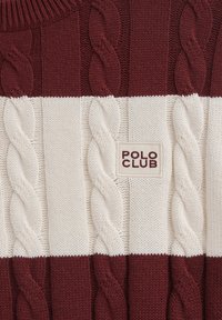Mörkröd och krämfärgad stickad tröja med kabelstickningsmönster, en ribbad halsringning och en "POLO CLUB" etikett på framsidan.
