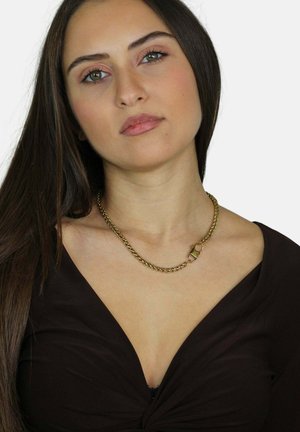 Collana in oro con maglie spesse e chiusura a lucchetto. Il modello indossa una maglia nera con scollatura a V, offrendo una chiara visione del gioiello.