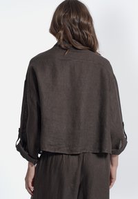 Giacca cropped in lino marrone con maniche arrotolate, tessuto leggero e vestibilità morbida. Presenta un colletto arrotondato e un design sul retro rilassato.