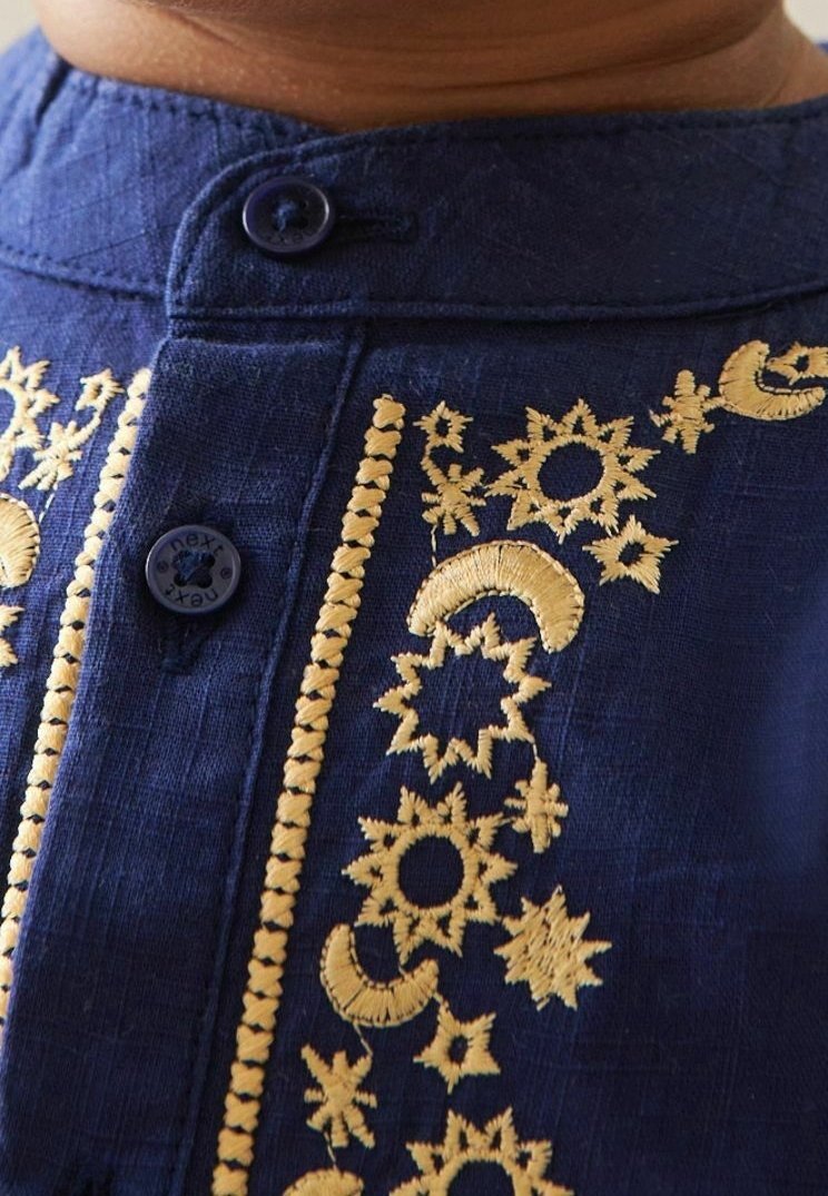 Gros plan sur le col d'une chemise bleu marine avec une broderie céleste jaune et deux boutons bleu foncé.