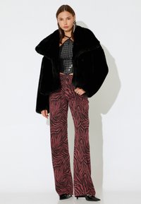 Veste en fausse fourrure noire, crop top en sequins argentés, et pantalon large à motifs zèbre rouge et noir, le tout complété par des escarpins noirs à bout pointu.